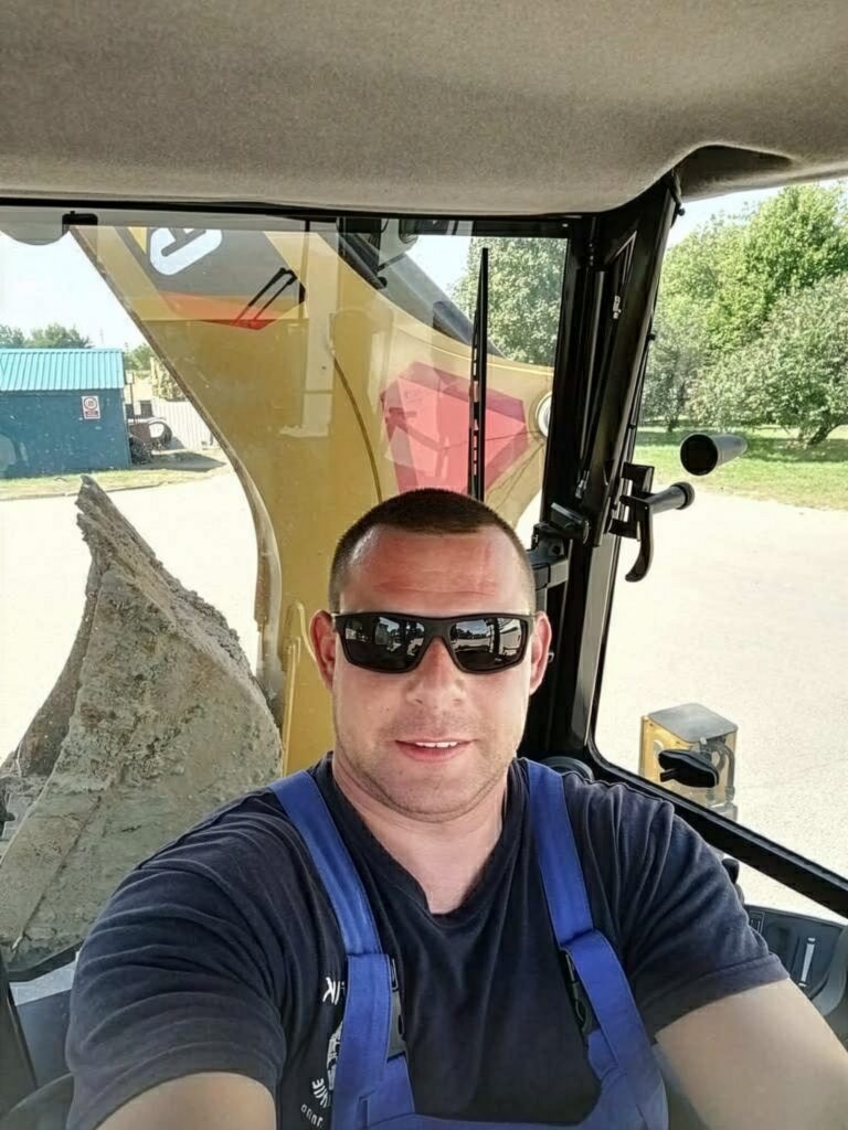 Kamil Bieda w okularach siedzi w kabinie koparki i pozuje do zdjęcia z bliskiego kadru.