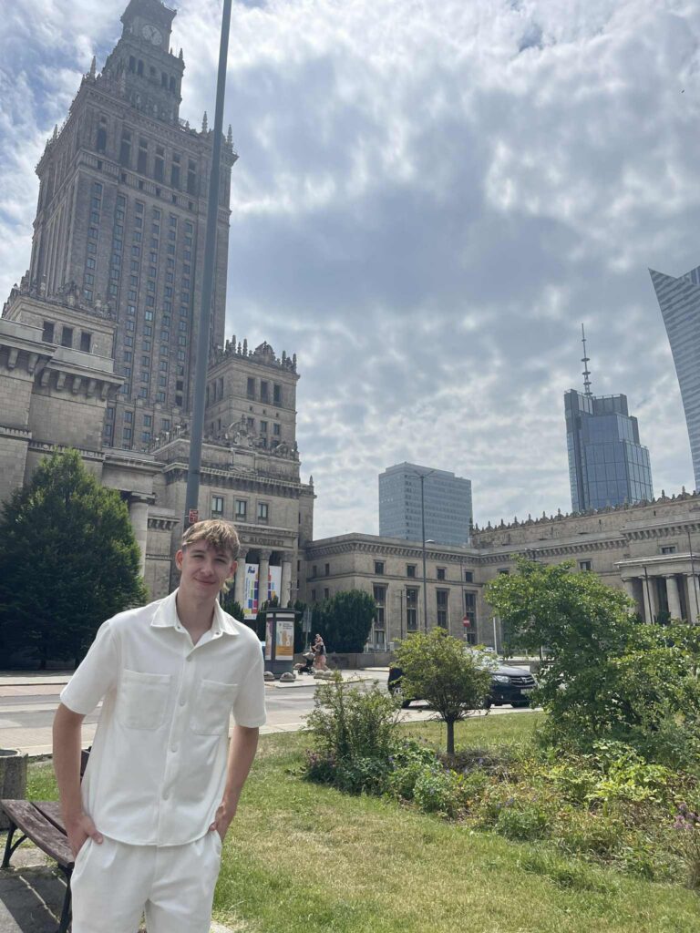 Mateusz Kata pozuje na tle Pałacu Kultury i Nauki.