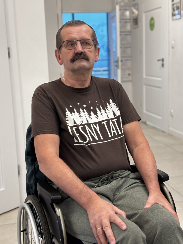 Ryszard Tokarzewski siedzi na wózku inwalidzkim i pozuje do zdjęcia w ośrodku neurorehabilitacji.