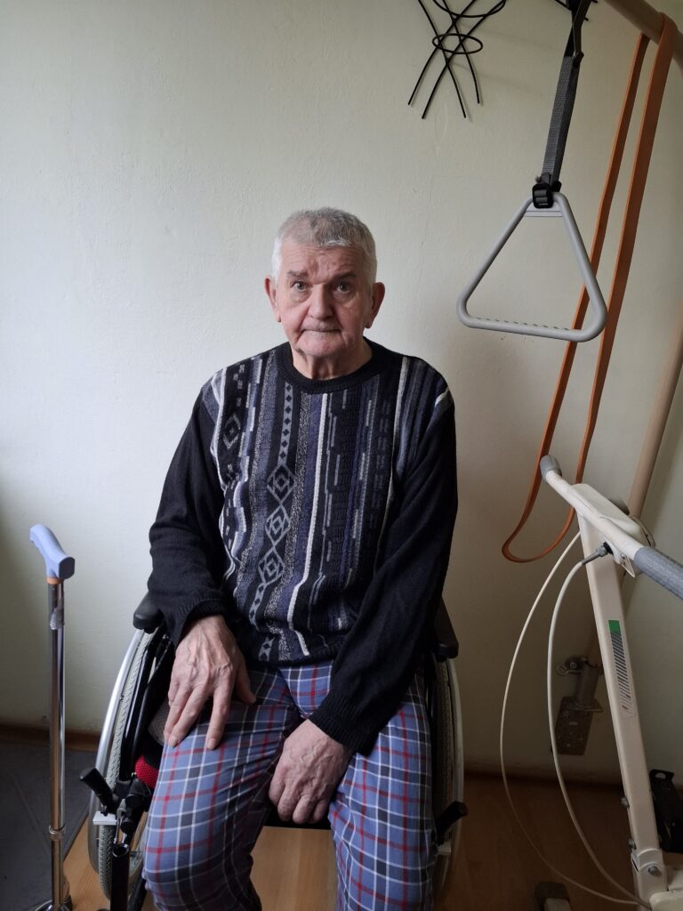 Wacław Ciurkiewicz pozuje do zdjęcia siedząc na wózku inwalidzkim.