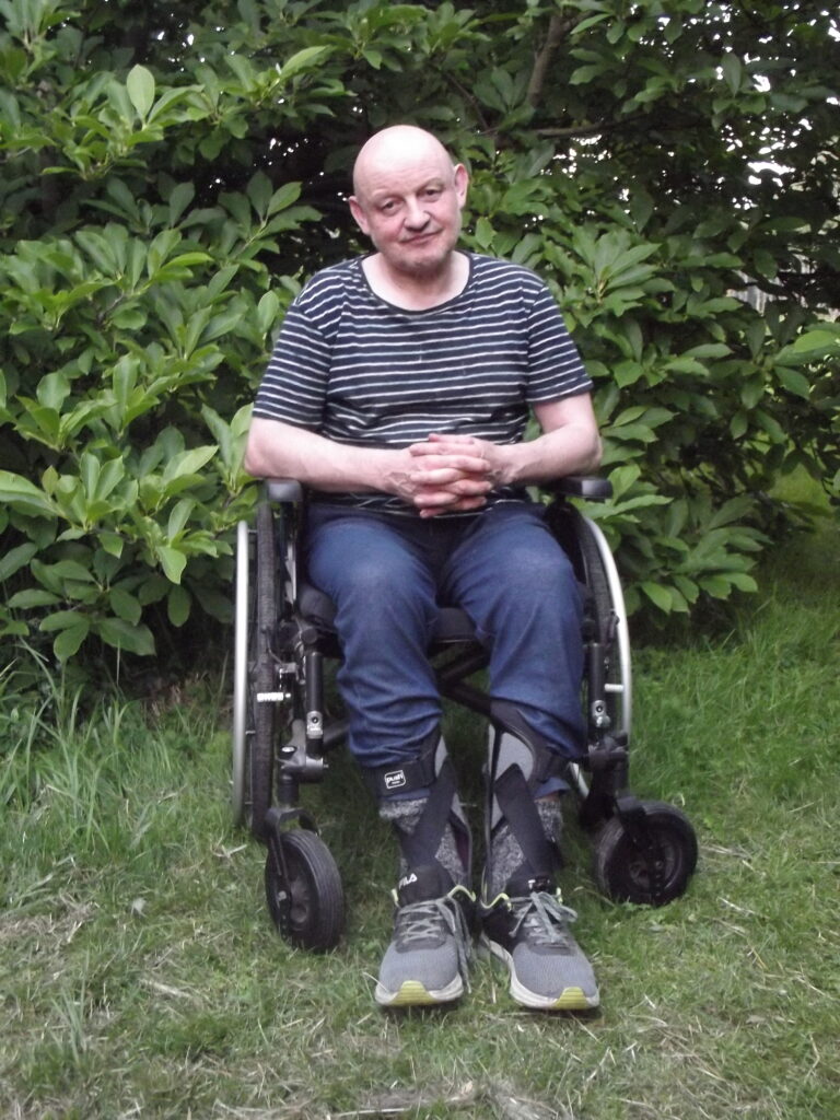 Kazimierz Szuster na wózku inwalidzkim pozuje do zdjęcia w ogrodzie.
