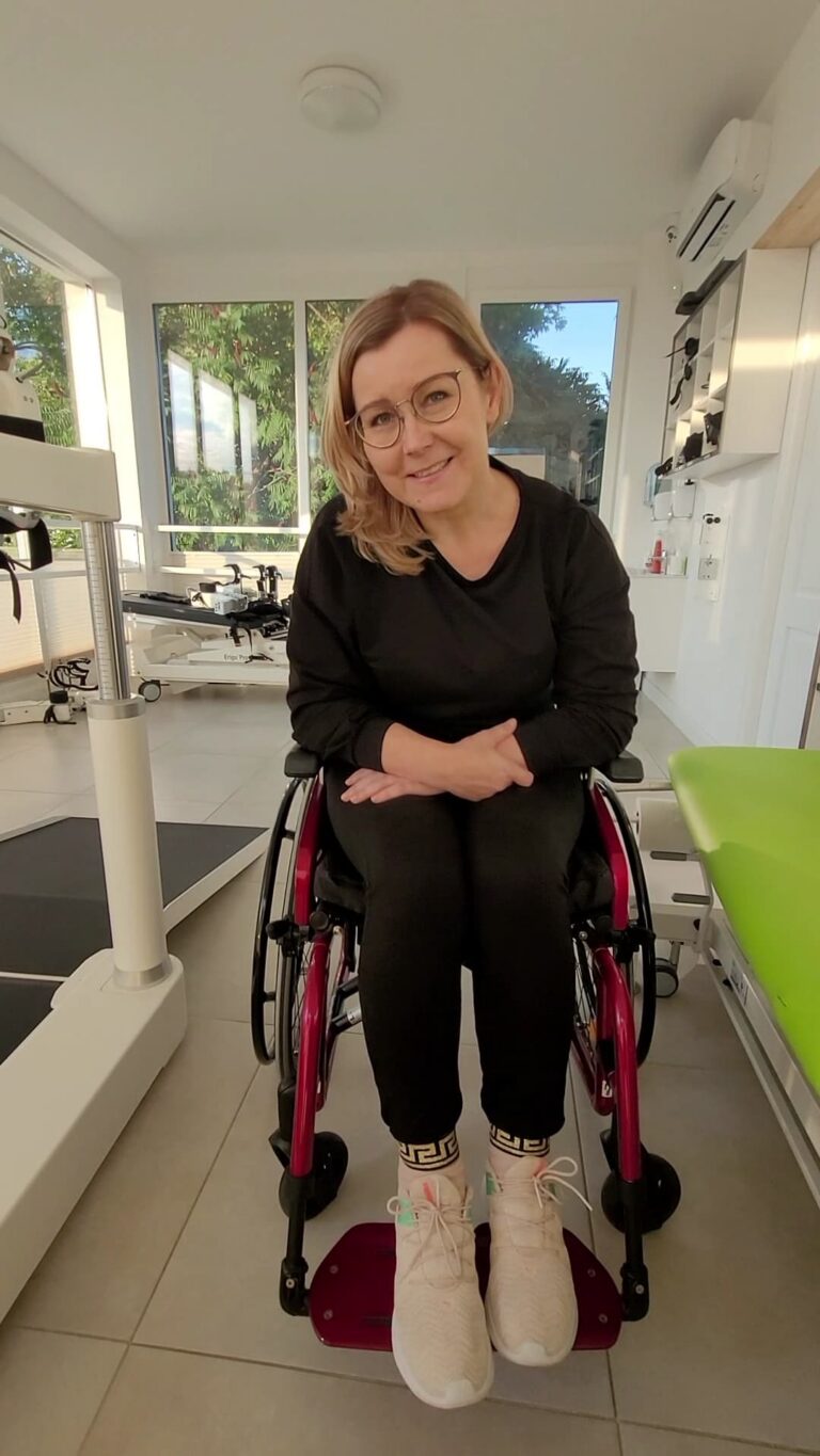 Agnieszka Krukowska uśmiecha się, siedząc w wózku aktywnym w jasnej sali.