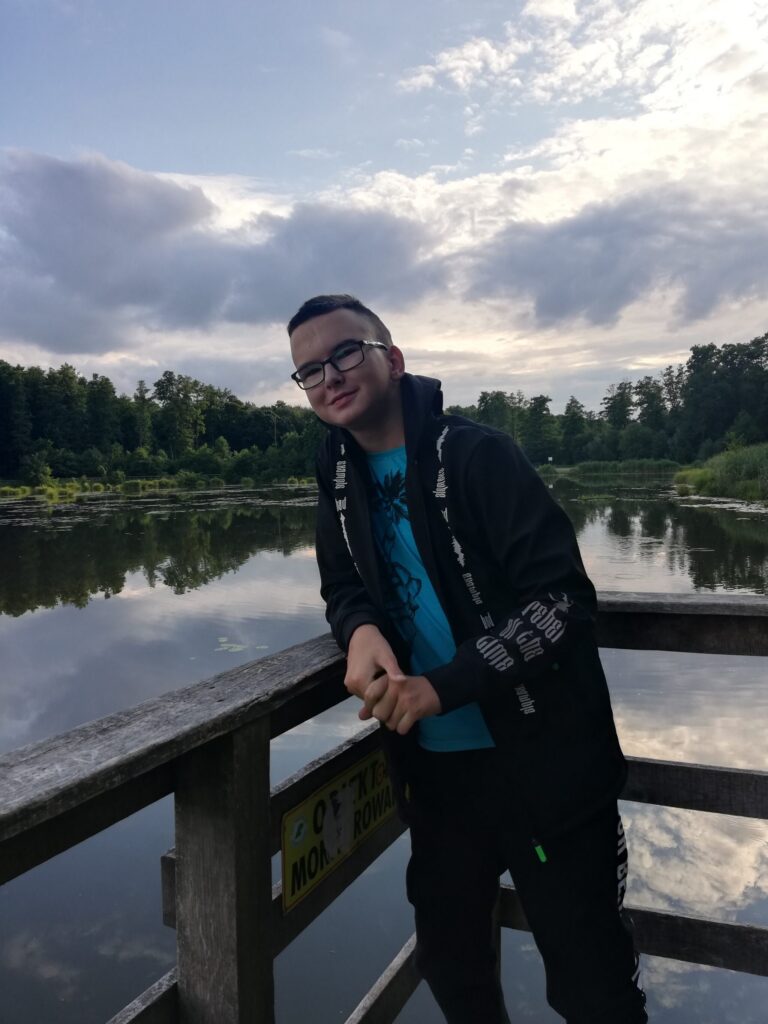 Aleksander Biały opiera się o barierkę pomostu nad stawem.