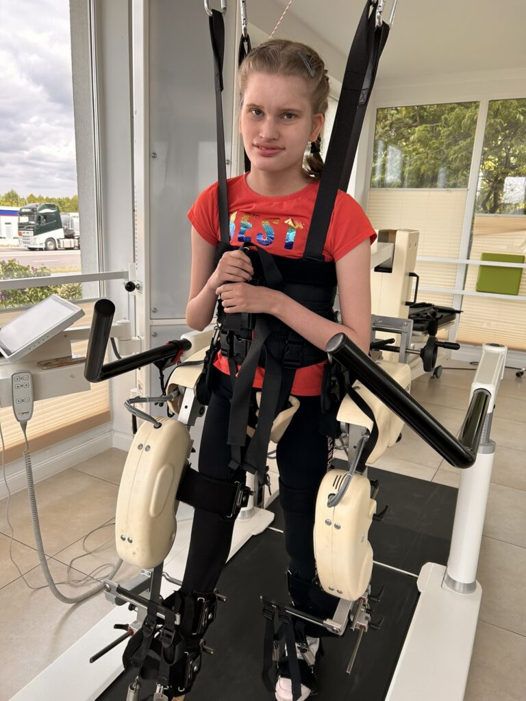 Aleksandra Błońska stoi zapięta w szelkach urządzenia do nauki chodu.