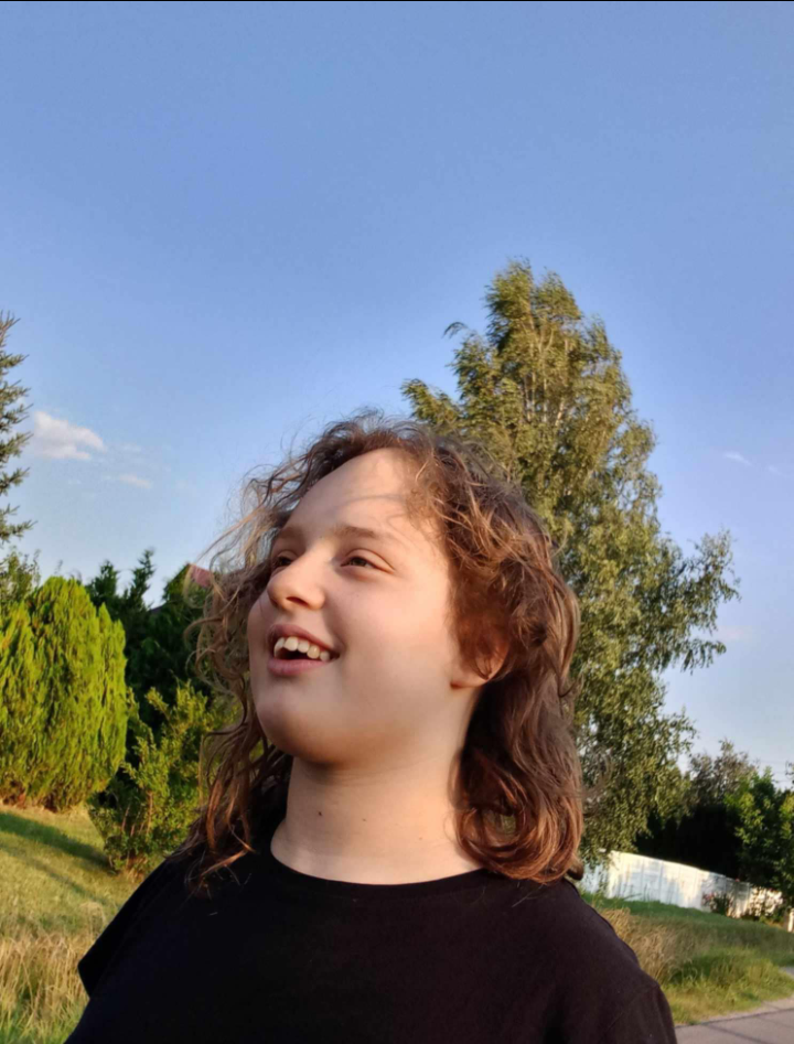 Amelia Kozar unosi głowę i szeroko się uśmiecha w ogrodzie o zachodzie słońca.
