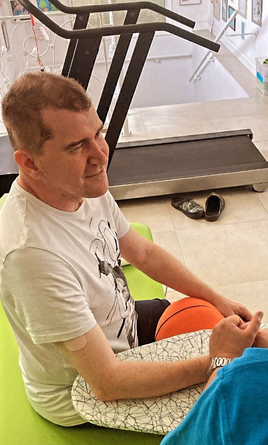 Dariusz Lewczuk siedzi na materacu w sali rehabilitacyjnej obok piłki do koszykówki.