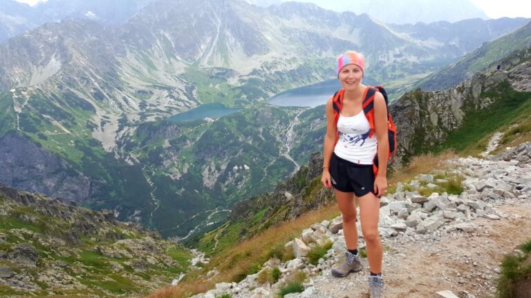 Edyta Lewtak stoi z plecakiem na kamienistym górskim szlaku nad doliną.