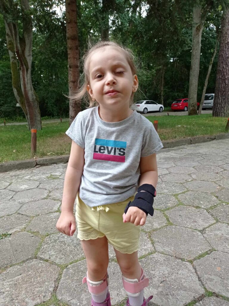 Gabrysia Belka stoi na alejce w parku, na prawej dłoni ma ortezę.