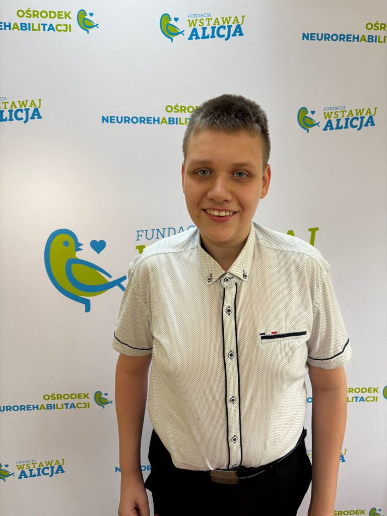 Jakub Dablowski uśmiecha się, stojąc przed ścianką z logotypami fundacji.