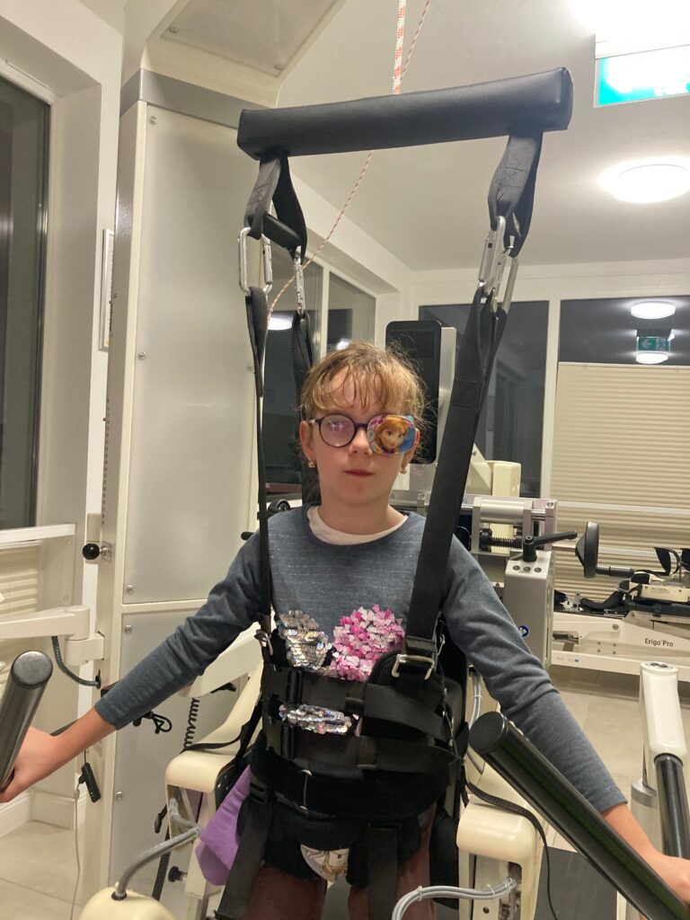 Marcelina Kruk stoi w uprzęży podwieszonej do ramy w sali rehabilitacyjnej.