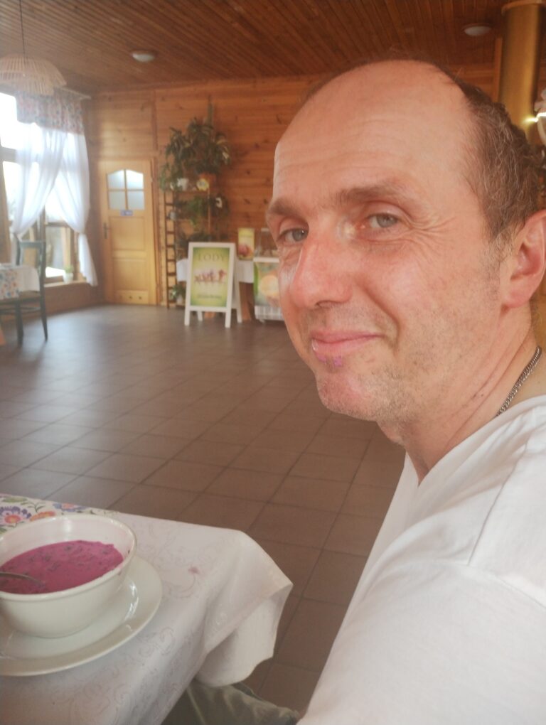 Marek Krzyżanowski siedzi przy nakrytym stole, przed nim talerz z zupą.
