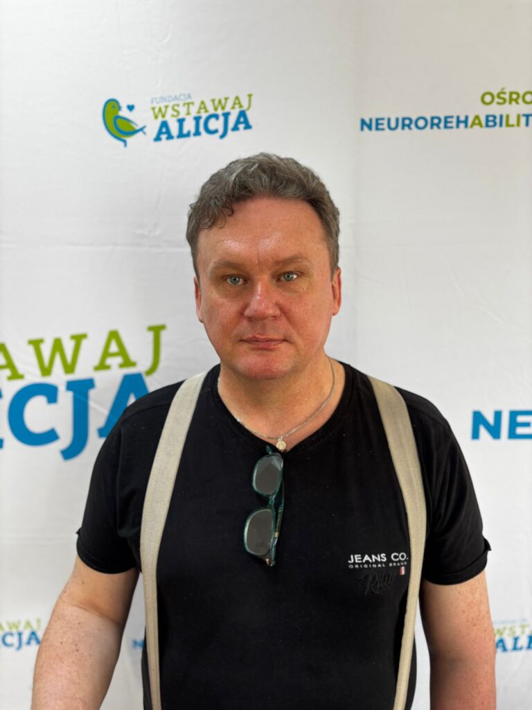 Mirosław Maksim stoi przed ścianką z logo fundacji.
