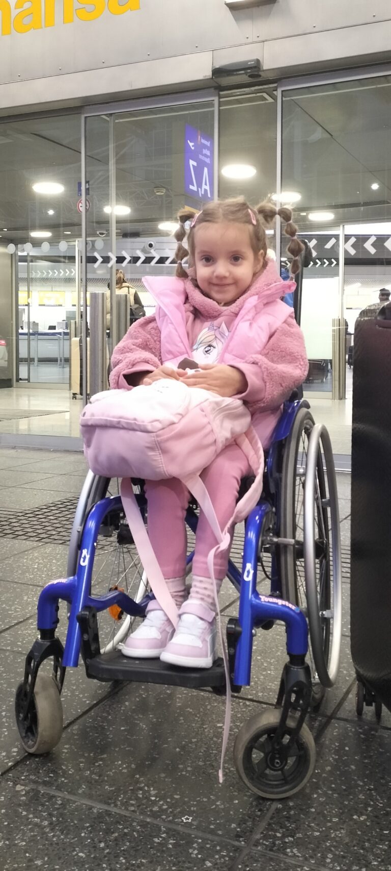 Oliwia Krauze siedzi w wózku w hali lotniska i trzyma torbę na kolanach.