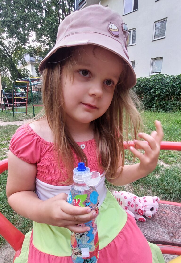 Oliwia Woźniak siedzi na konstrukcji na placu zabaw i trzyma butelkę wody.