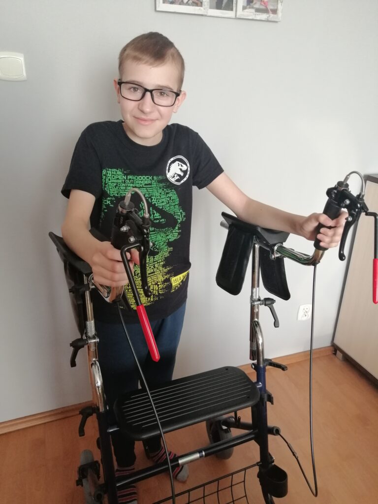 Patryk Klej stoi przy podpórce do chodzenia i trzyma jej uchwyty.
