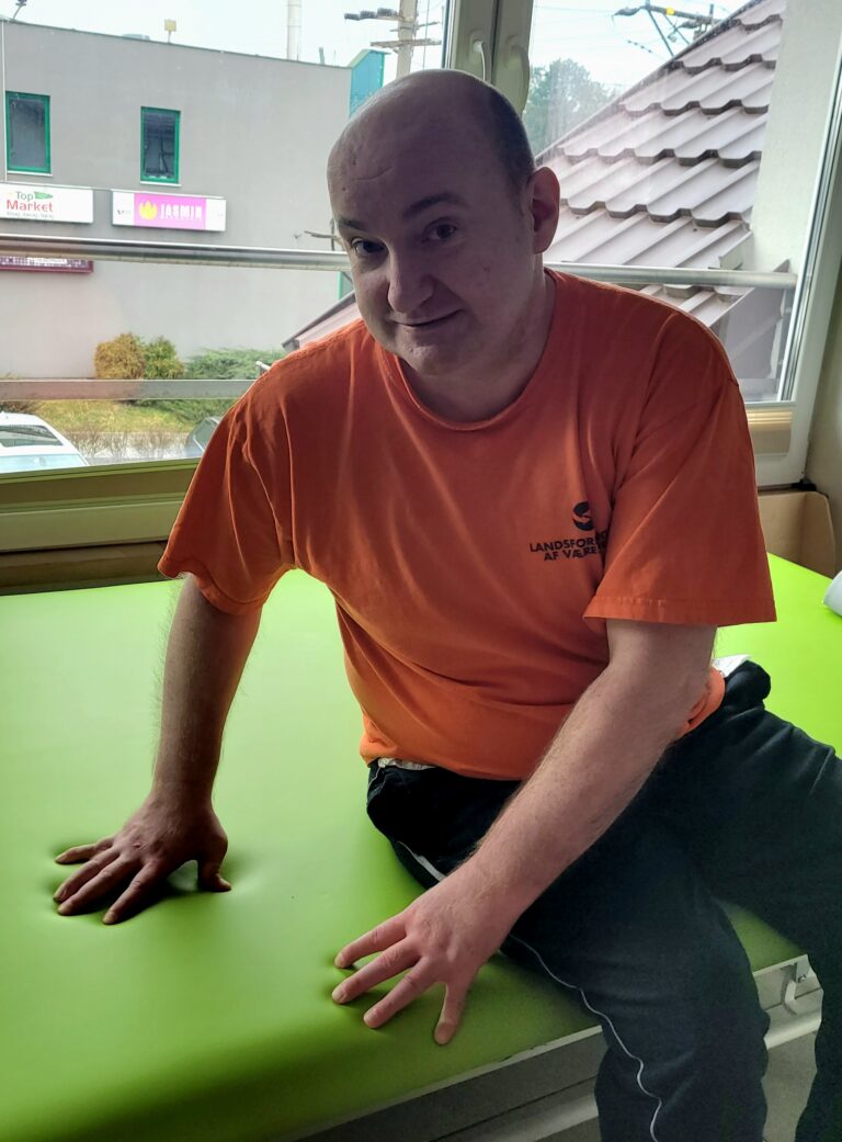 Piotr Piotrowski siedzi na macie rehabilitacyjnej i opiera o nią dłonie.