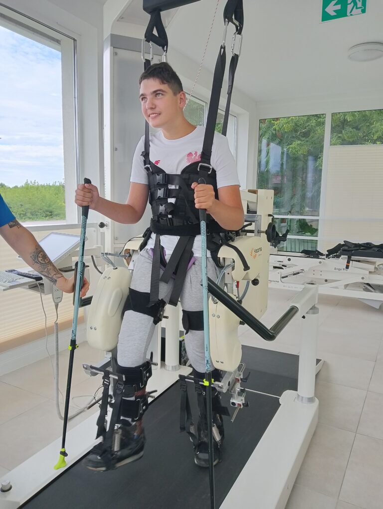 Sebastian Krupa stoi w uprzęży nad bieżnią i trzyma dwie kule.