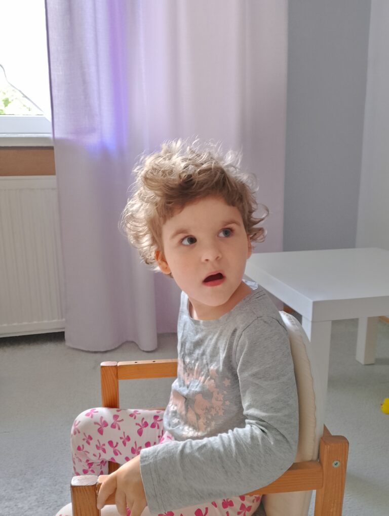 Zuzanna Garbala siedzi na małym drewnianym krzesełku i patrzy w obiektyw.