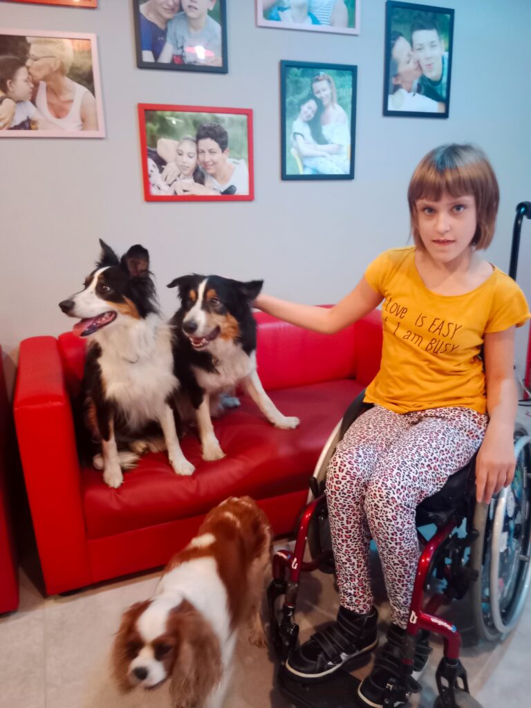 Zuzanna Ostrowska wyciąga rękę do psów, siedząc w wózku.