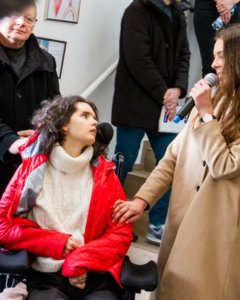 Alicja na wózku podczas otwarcia Ośrodka, przyjaciółka śpiewa jej do mikrofonu