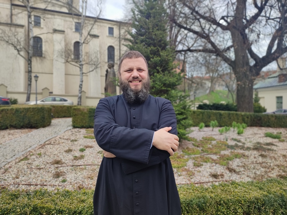 Ksiądz Emil Mazur pozuje ze skrzyżowanymi rękami na tle Katedry Lubelskiej.